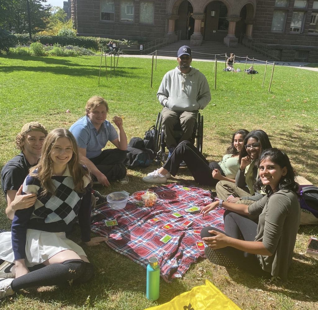 Seven students, including Catherine, smiling and sitting around a picnic blanket on the Victoria College quad.